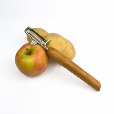 Ein Pendelschäler aus Erle auf einem Apfel und zwei Kartoffeln. 